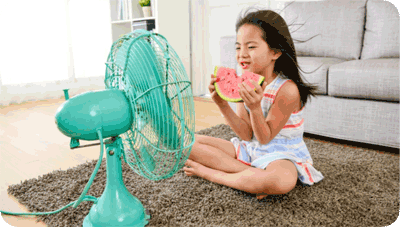 A young girl eating watermelon staying cool beside a fan